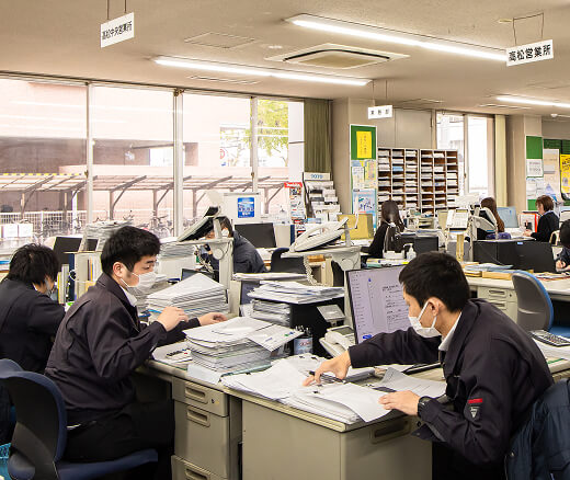 事務所内で、資料を見ながら仕事をしているスタッフ達